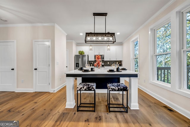 kitchen featuring appliances with stainless steel finishes, a kitchen breakfast bar, tasteful backsplash, light hardwood / wood-style flooring, and white cabinetry