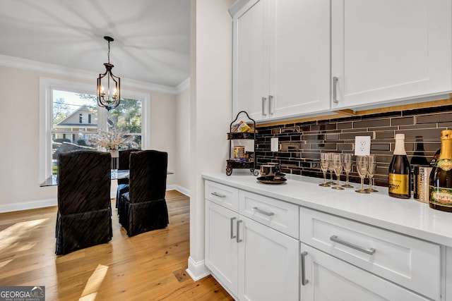 bar with light wood-type flooring, tasteful backsplash, ornamental molding, decorative light fixtures, and white cabinetry