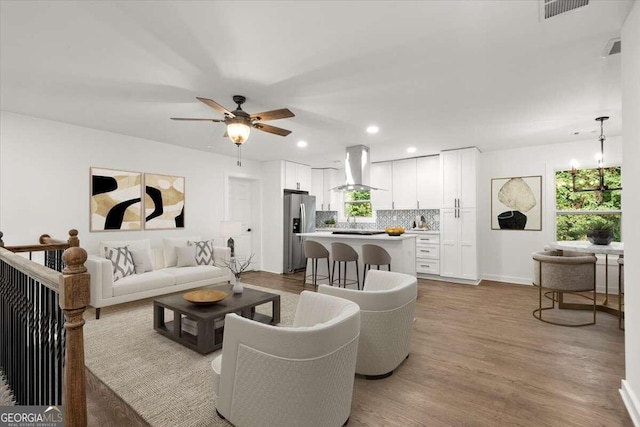 living room with ceiling fan with notable chandelier and light wood-type flooring