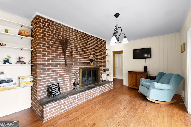 living room featuring a brick fireplace, ornamental molding, hardwood / wood-style flooring, and an inviting chandelier