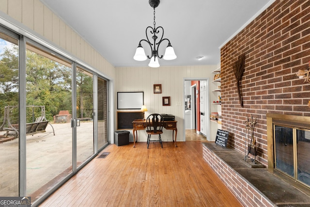 office area featuring wood-type flooring, a notable chandelier, a brick fireplace, and brick wall