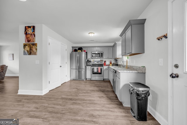 kitchen with light hardwood / wood-style floors, sink, light stone counters, appliances with stainless steel finishes, and gray cabinets