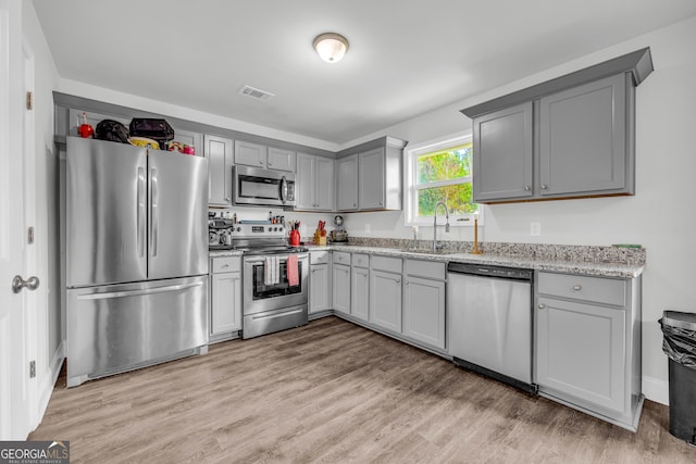 kitchen with stainless steel appliances, sink, light stone counters, gray cabinetry, and light wood-type flooring