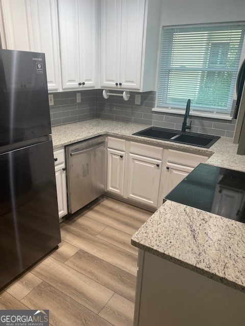 kitchen with light stone counters, white cabinets, black appliances, sink, and light wood-type flooring