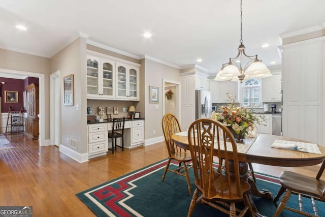 dining space with light wood-style flooring, baseboards, built in desk, and ornamental molding