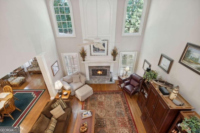 living room featuring a fireplace, a towering ceiling, wood finished floors, a ceiling fan, and ornate columns