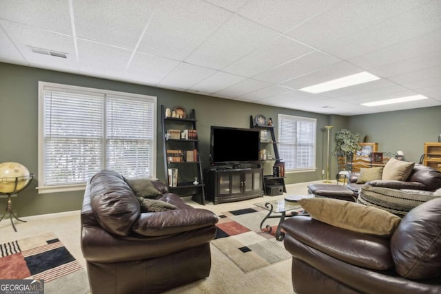 living room with a wealth of natural light, visible vents, baseboards, and a drop ceiling