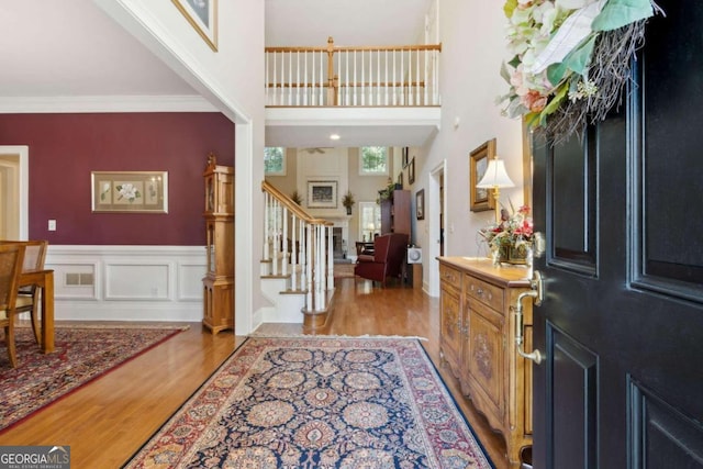 entrance foyer with stairs, light wood-style floors, wainscoting, crown molding, and a decorative wall
