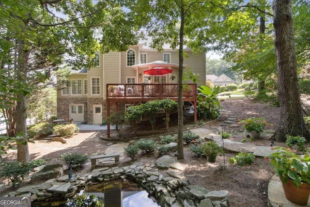 back of house featuring a wooden deck, stone siding, and a patio area