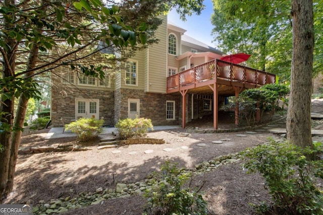 back of property featuring a wooden deck, stone siding, french doors, and a patio area