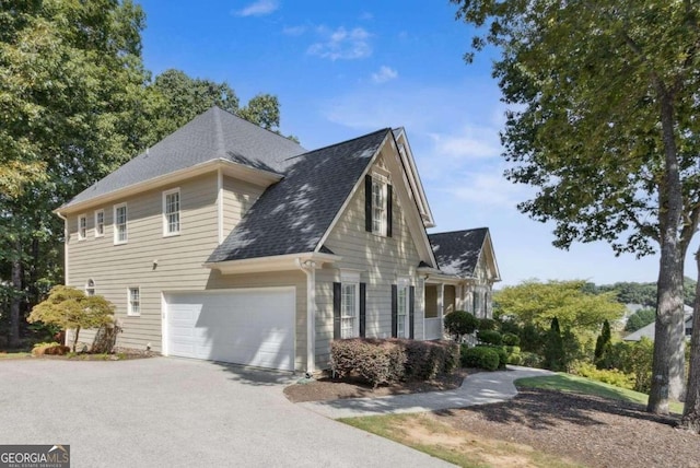 view of side of property featuring a garage, driveway, and a shingled roof