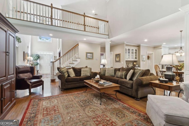 living area with a towering ceiling, wood finished floors, stairs, and ornate columns