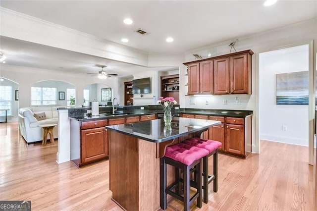 kitchen with ornamental molding, a center island, a kitchen breakfast bar, dark stone countertops, and light hardwood / wood-style flooring