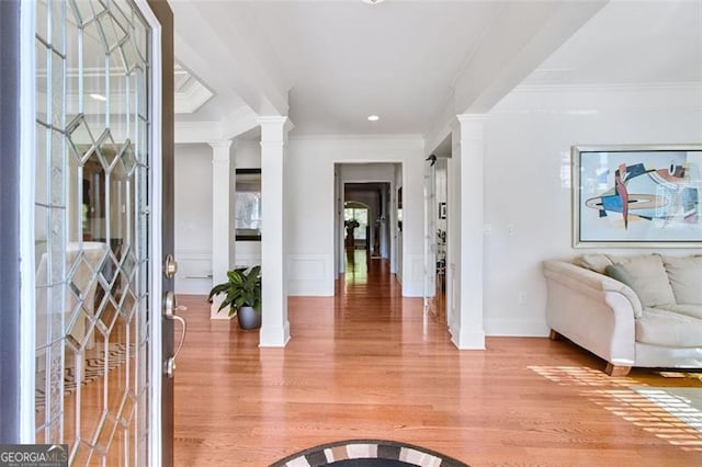 entryway with light hardwood / wood-style floors, crown molding, and decorative columns