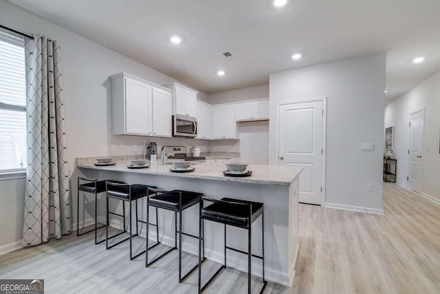 kitchen featuring a breakfast bar, white cabinetry, light hardwood / wood-style flooring, appliances with stainless steel finishes, and kitchen peninsula