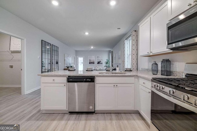 kitchen featuring sink, white cabinets, stainless steel appliances, light stone countertops, and light hardwood / wood-style flooring