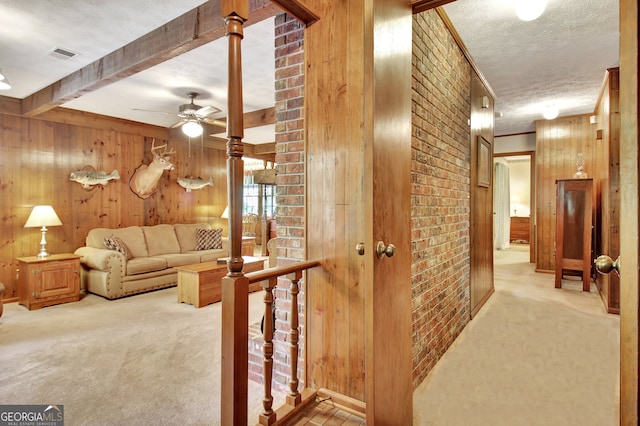 carpeted living room featuring wood walls, beamed ceiling, and a textured ceiling