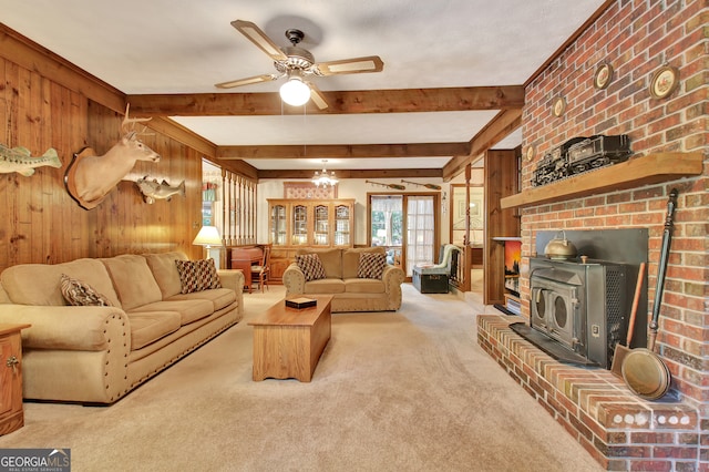 living room featuring beamed ceiling, wooden walls, a wood stove, and light colored carpet