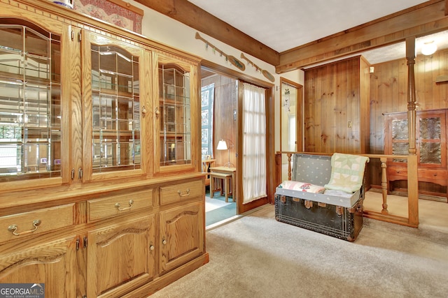 living area with wooden walls, light carpet, and beam ceiling