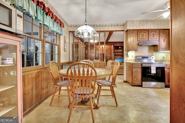 dining area with ceiling fan with notable chandelier and wood walls