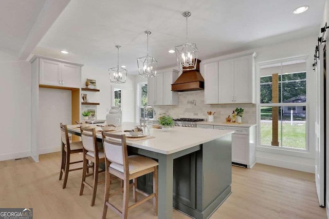 kitchen with white cabinets, an island with sink, a barn door, and premium range hood