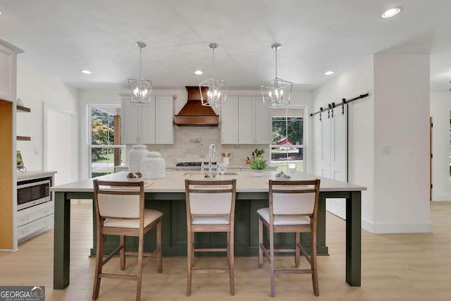 kitchen featuring a barn door, hanging light fixtures, white cabinetry, and custom exhaust hood