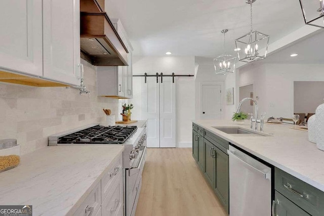 kitchen featuring stainless steel appliances, sink, custom exhaust hood, a barn door, and pendant lighting