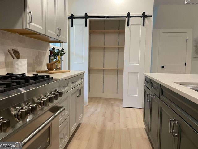 kitchen featuring high end stainless steel range, tasteful backsplash, a barn door, and light hardwood / wood-style floors