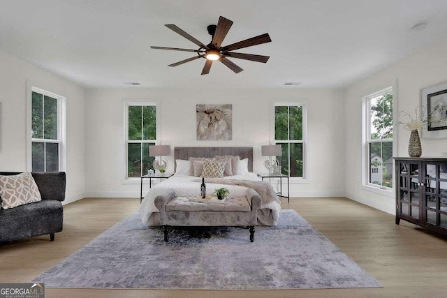 bedroom with multiple windows, light hardwood / wood-style floors, and ceiling fan