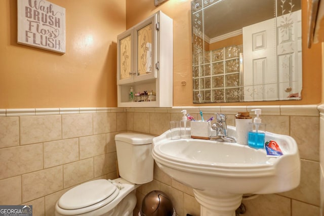 bathroom with toilet, ornamental molding, sink, and tile walls