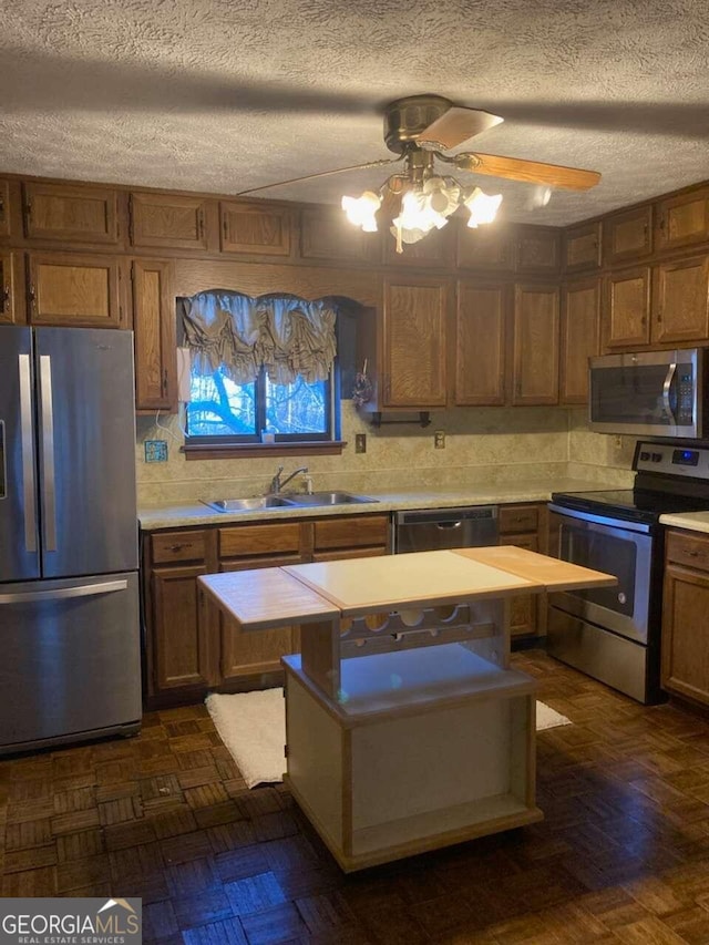 kitchen featuring stainless steel appliances, ceiling fan, a textured ceiling, sink, and dark parquet flooring