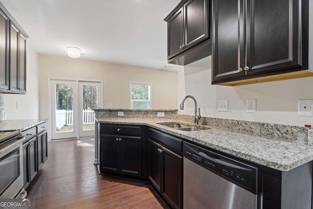 kitchen with sink, kitchen peninsula, appliances with stainless steel finishes, light stone countertops, and dark wood-type flooring