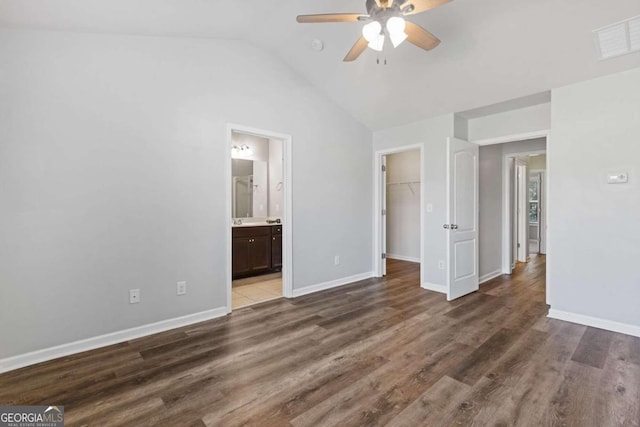 unfurnished bedroom featuring dark hardwood / wood-style flooring, lofted ceiling, ceiling fan, a closet, and a walk in closet