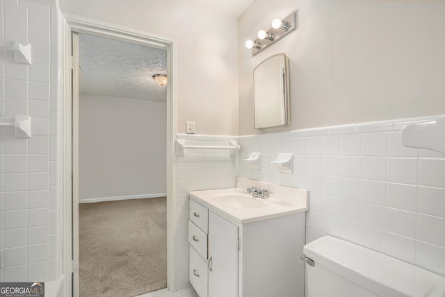 bathroom featuring toilet, vanity, tile walls, and a textured ceiling