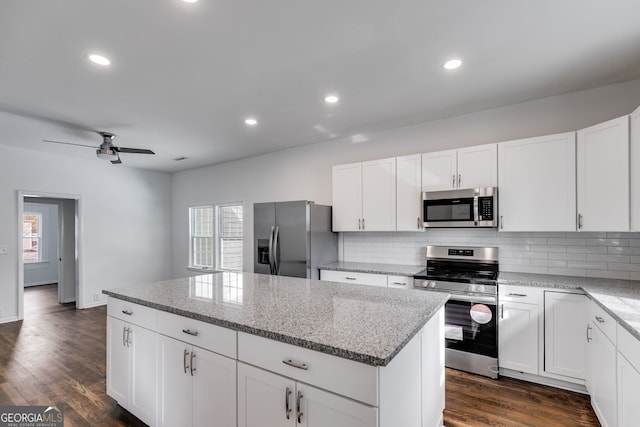 kitchen featuring light stone countertops, appliances with stainless steel finishes, white cabinetry, and a center island