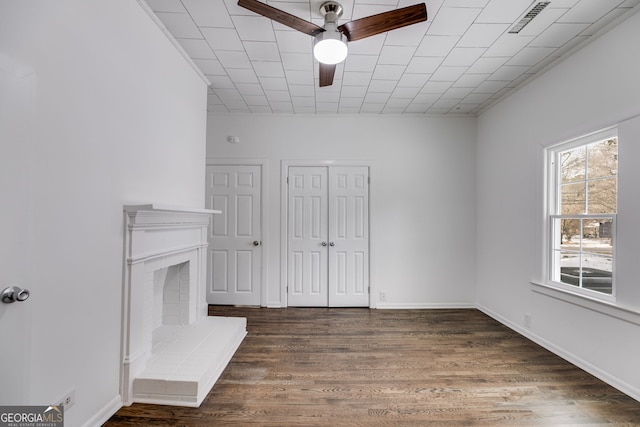 unfurnished living room with a brick fireplace, dark hardwood / wood-style flooring, and ceiling fan