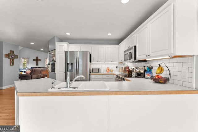 kitchen with kitchen peninsula, white cabinets, sink, and appliances with stainless steel finishes