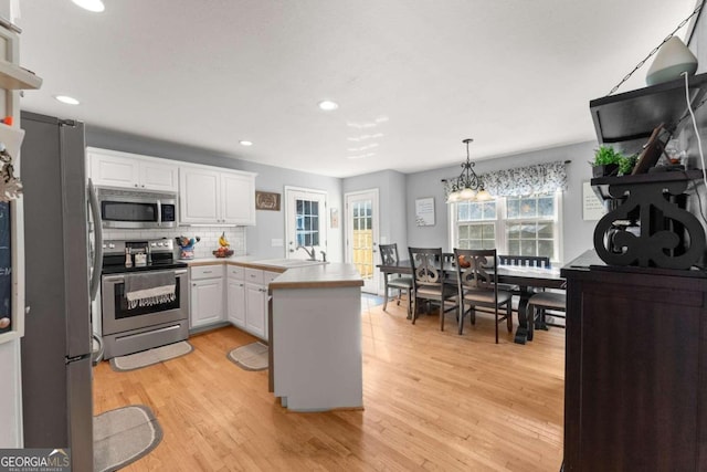 kitchen with stainless steel appliances, light wood-type flooring, white cabinetry, hanging light fixtures, and kitchen peninsula