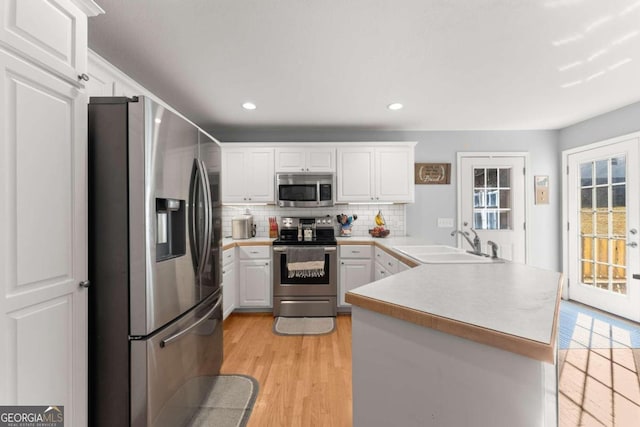 kitchen featuring stainless steel appliances, white cabinets, kitchen peninsula, sink, and light hardwood / wood-style flooring