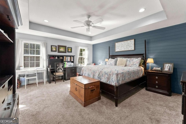 bedroom with light colored carpet, ceiling fan, wooden walls, and a tray ceiling