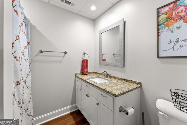 bathroom with a paneled ceiling, wood-type flooring, toilet, and vanity