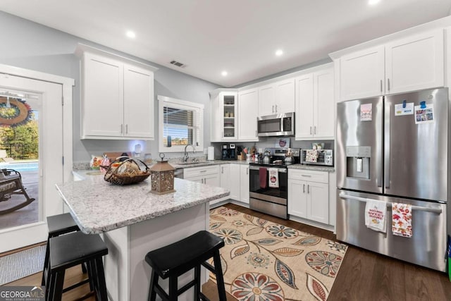 kitchen with white cabinetry, stainless steel appliances, a breakfast bar, and light stone countertops