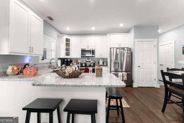 kitchen with dark hardwood / wood-style flooring, appliances with stainless steel finishes, a kitchen bar, and white cabinets