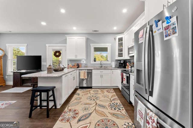 kitchen with white cabinetry, appliances with stainless steel finishes, dark hardwood / wood-style flooring, light stone countertops, and a breakfast bar area