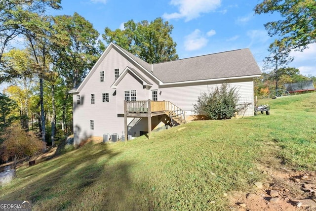 rear view of property featuring a lawn, a wooden deck, and central AC