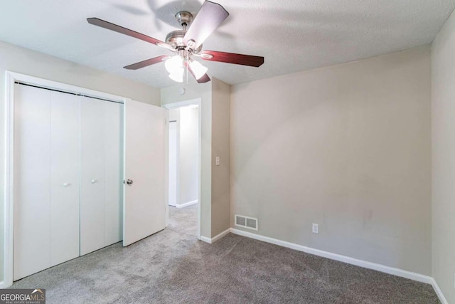 unfurnished bedroom with light carpet, ceiling fan, a textured ceiling, and a closet