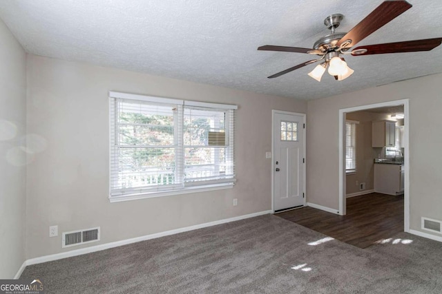 entrance foyer featuring a wealth of natural light, ceiling fan, dark colored carpet, and a textured ceiling