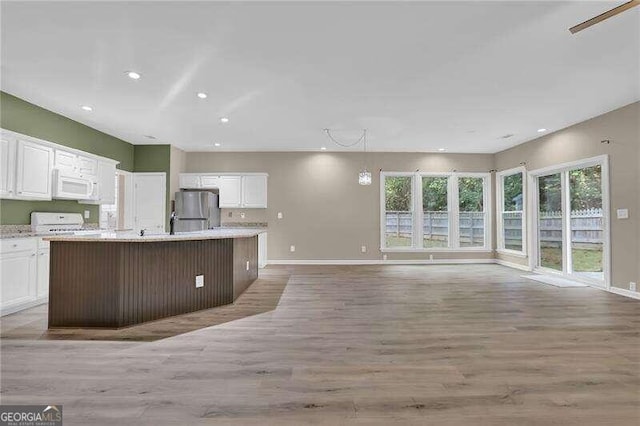 kitchen with white cabinets, hanging light fixtures, a kitchen island with sink, light wood-type flooring, and white appliances