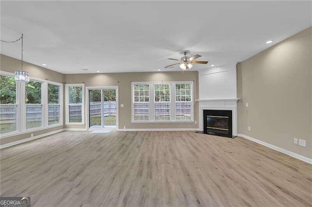 unfurnished living room with light hardwood / wood-style floors, ceiling fan with notable chandelier, and a large fireplace