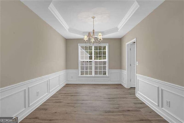 unfurnished dining area featuring a chandelier, a raised ceiling, light wood-type flooring, and crown molding